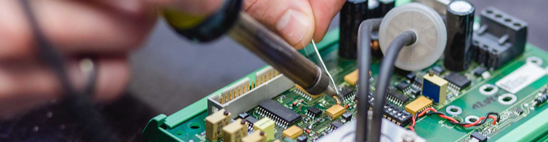 Hände mit Lötgerät an einer Platine