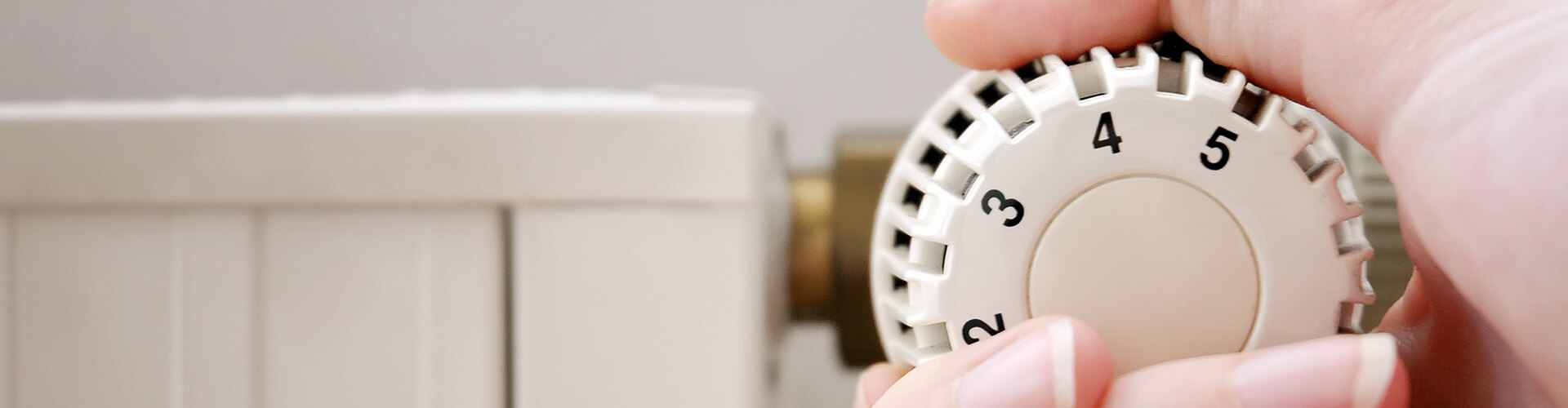 Hand dreht am Thermostat einer Heizung